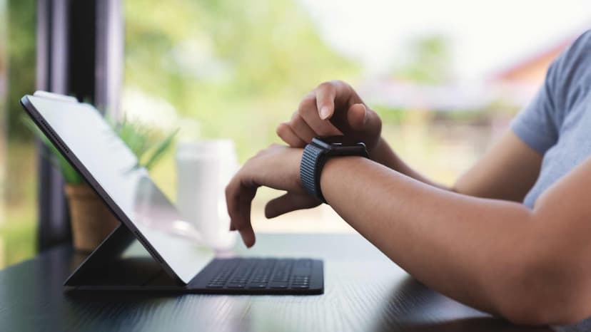 Male sitting in front of laptop checking a notification on smartwatch