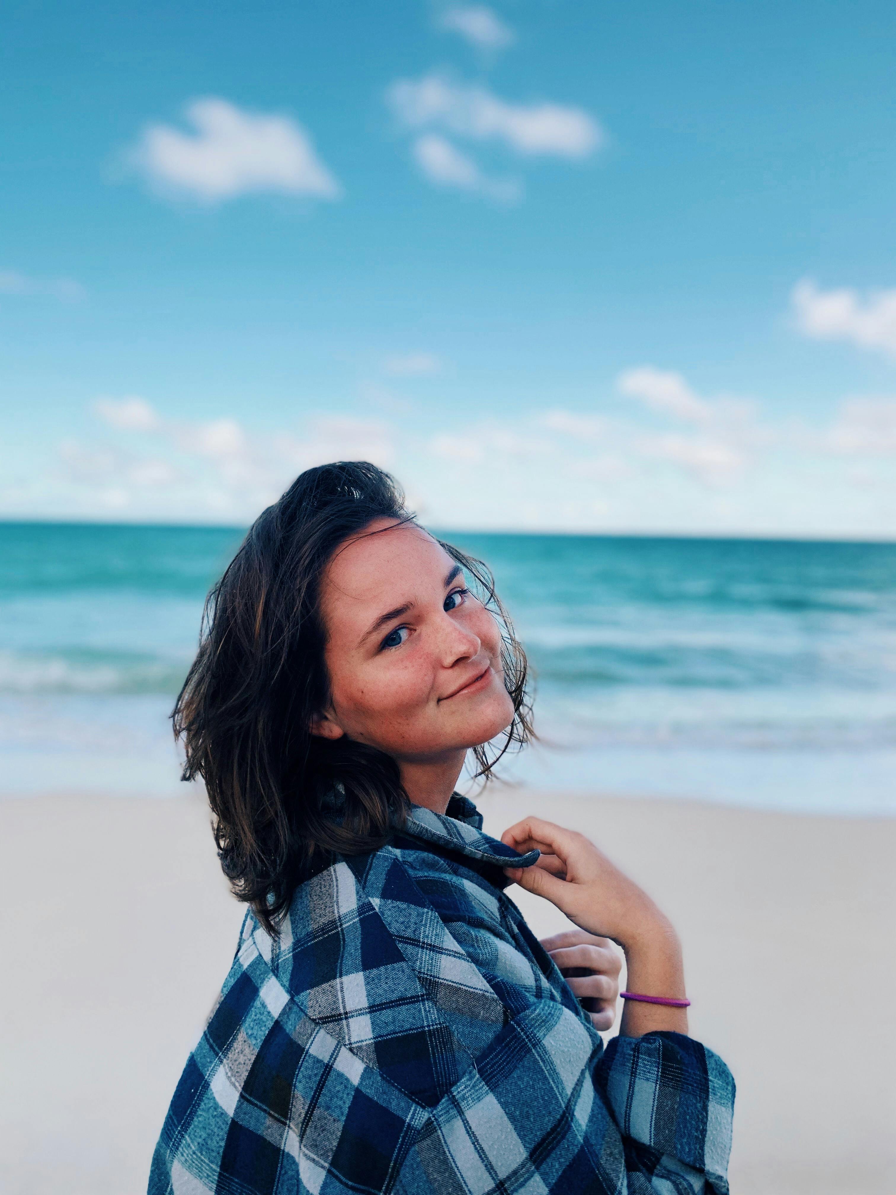 Female wearing flannel smiling at the camera while on the beach