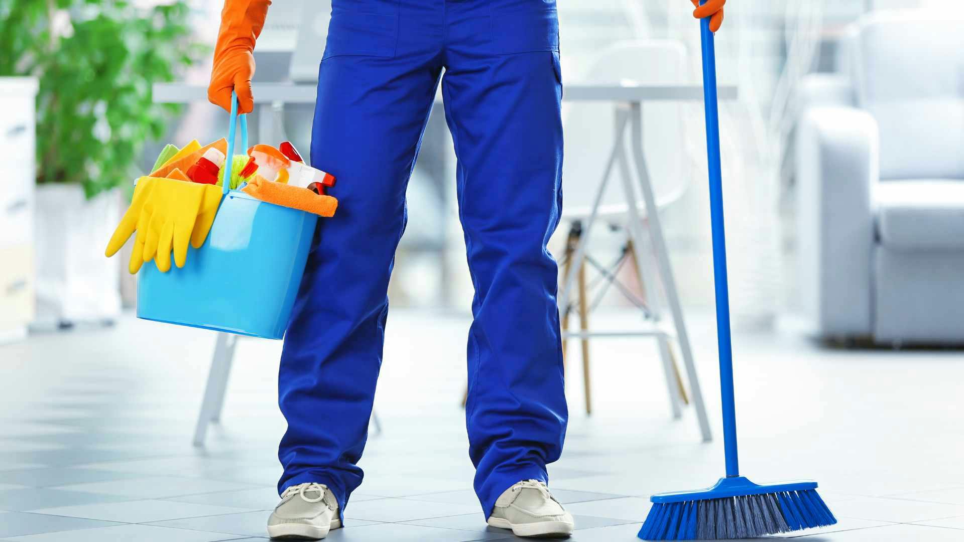Residential cleaner holding a cleaning caddy in one hand and then a broom in the other