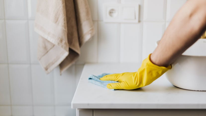 cleaners gloved hand using a microfiber cloth to clean the bathroom counter