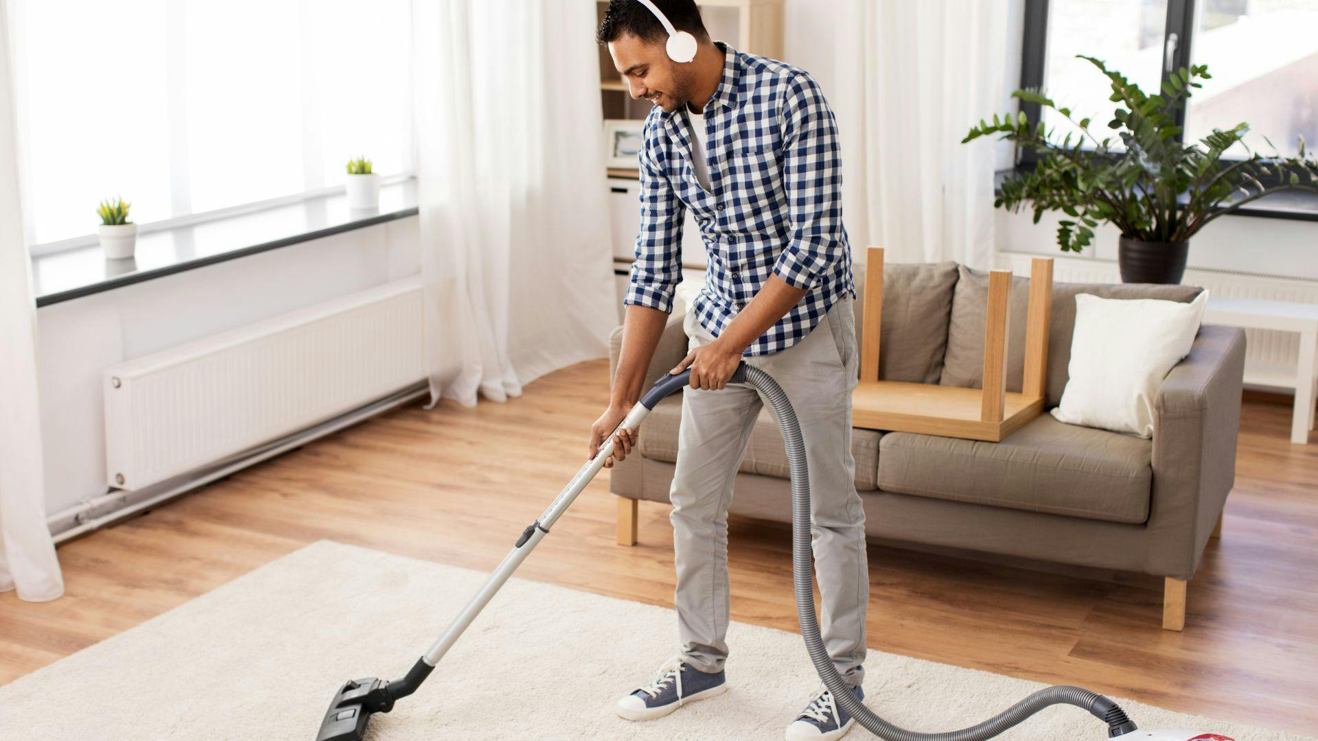 Male field service cleaner wearing headphones as he vacuums rug in living room