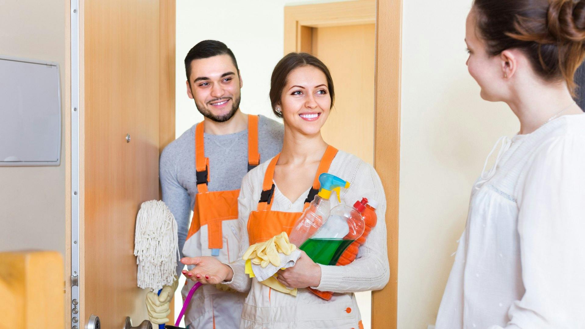 House cleaners being welcomed in to a home by homeowner while holding cleaning supplies