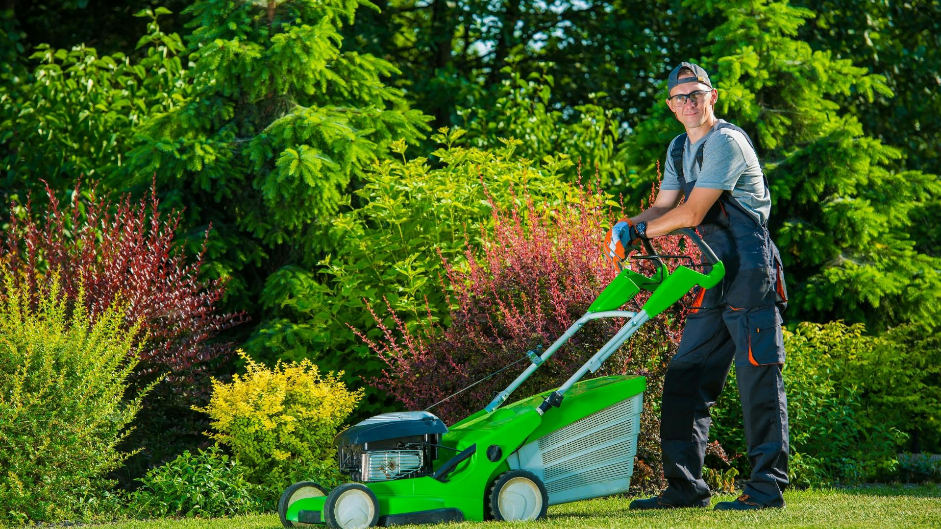 Lawn care employee leaning on lawn mower and smiling