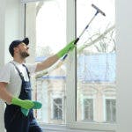 A man smiling as he cleans the windows from inside a home