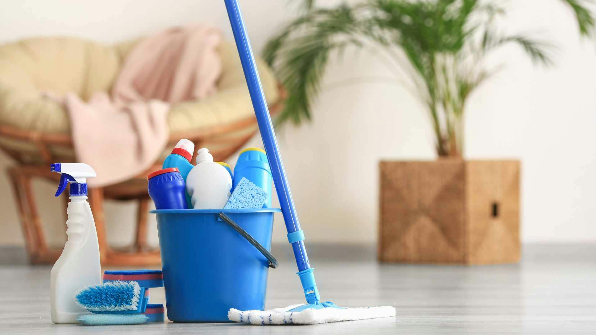 Mop next to bucket of cleaning supplies with a spray bottle and sponge to the right of the bucket