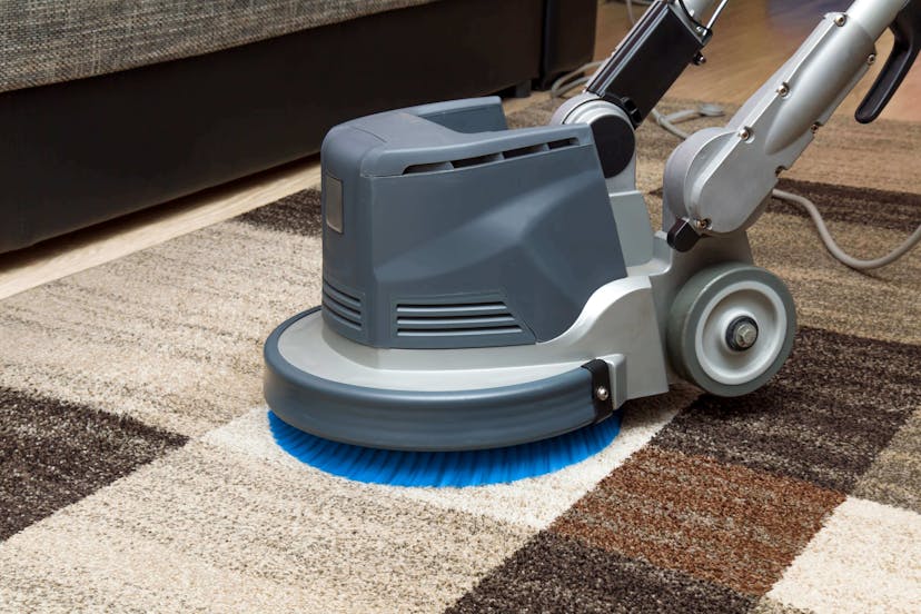 Carpet cleaner equipment on brown checkered rug in a large room.