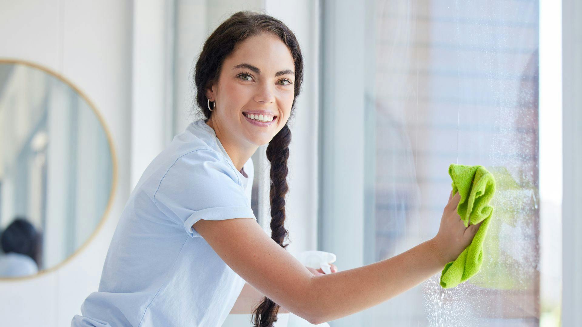 Professional window washer using a microfiber cloth to clean windows and smiling